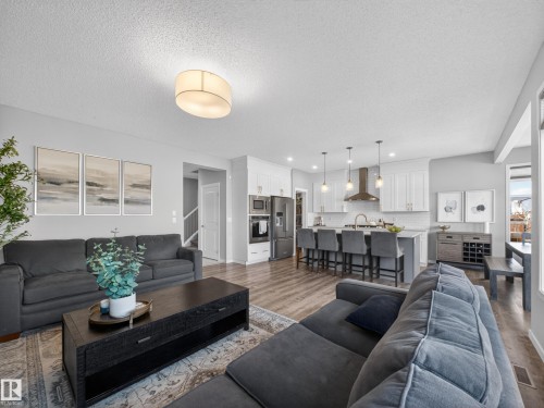 Open-concept living space featuring wood-look flooring, a kitchen island with seating, a stainless steel range hood, and white cabinetry - 3210 Chernowski Way, Edmonton, AB - Indoor Photo Showing Living Room