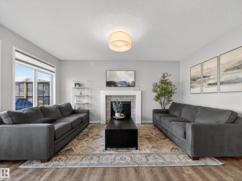 The living room features hardwood style flooring, a central area rug, and a fireplace with a white mantel and light-toned tile surround - 3210 Chernowski Way, Edmonton, AB - Indoor Photo Showing Living Room With Fireplace