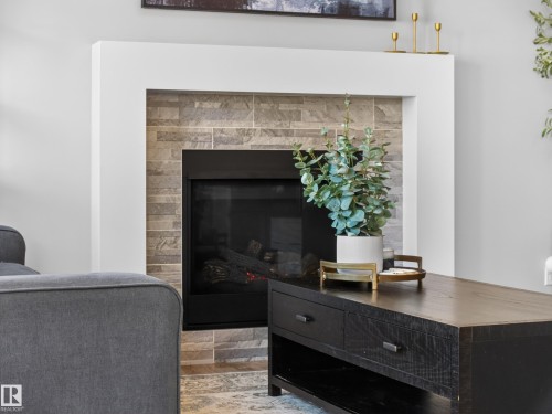 Living area featuring a modern fireplace with a light-colored surround and stone tile accents - 3210 Chernowski Way, Edmonton, AB - Indoor Photo Showing Living Room With Fireplace