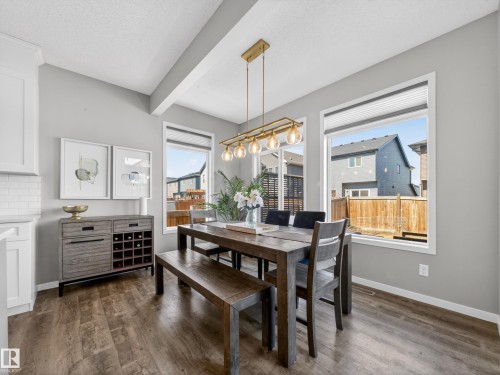 The dining area features engineered hardwood flooring, a gold-toned chandelier, and three windows providing natural light - 3210 Chernowski Way, Edmonton, AB - Indoor Photo Showing Dining Room