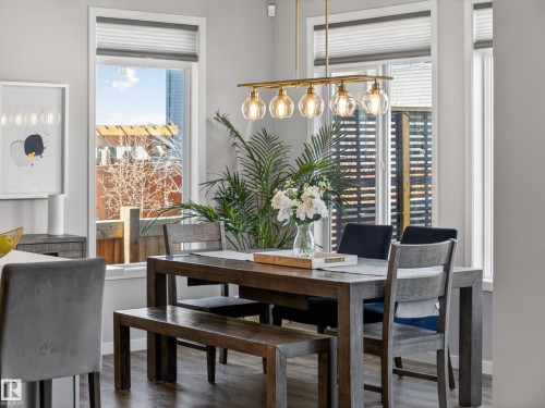 Dining area featuring a modern linear chandelier with four glass globes, large windows, and a dark-toned dining table with matching seating - 3210 Chernowski Way, Edmonton, AB - Indoor Photo Showing Dining Room