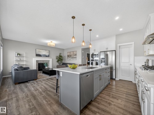 The property features an open-concept living area with a kitchen island, stainless steel appliances, and a fireplace in the living room - 3210 Chernowski Way, Edmonton, AB - Indoor Photo Showing Kitchen With Stainless Steel Kitchen With Upgraded Kitchen