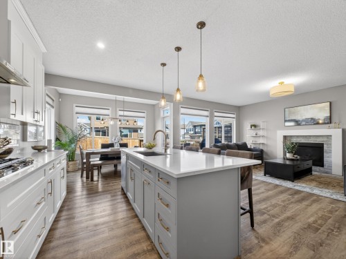Open concept living space featuring a kitchen island with a sink, pendant lighting, and a living area with a fireplace - 3210 Chernowski Way, Edmonton, AB - Indoor Photo Showing Kitchen With Upgraded Kitchen