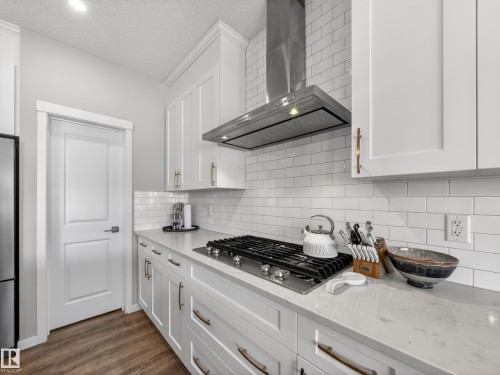 The kitchen features white cabinetry, a gas range with a stainless steel range hood, white subway tile backsplash, and light-colored countertops - 3210 Chernowski Way, Edmonton, AB - Indoor Photo Showing Kitchen With Upgraded Kitchen