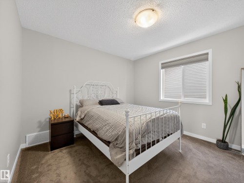 The room features light gray walls, a window with blinds, and a textured ceiling with a flush-mount light fixture - 3210 Chernowski Way, Edmonton, AB - Indoor Photo Showing Bedroom