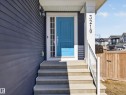 The property features a bold blue front door, concrete steps with a white handrail, and siding in a dark blue hue - 3210 Chernowski Way, Edmonton, AB  - Outdoor With Exterior 