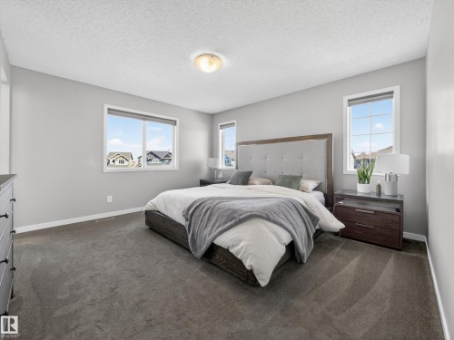 This bedroom features light gray walls, gray carpeting, and multiple windows providing natural light - 3210 Chernowski Way, Edmonton, AB - Indoor Photo Showing Bedroom