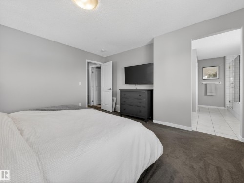 The bedroom features plush carpeting, light gray walls, and an overhead light fixture, with a doorway leading to a bathroom that includes tiled flooring and a glass-enclosed shower - 3210 Chernowski Way, Edmonton, AB - Indoor Photo Showing Bedroom