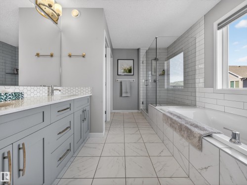 Well-appointed bathroom featuring a double vanity with grey cabinetry, a spacious bathtub, and a separate shower with a clear glass enclosure - 3210 Chernowski Way, Edmonton, AB - Indoor Photo Showing Bathroom
