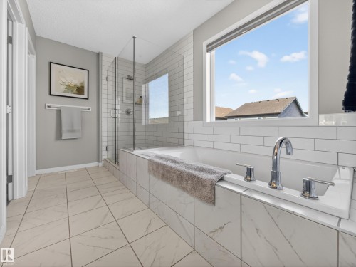 The bathroom features a spacious bathtub with a chrome faucet, a glass-enclosed shower, and a large window providing natural light - 3210 Chernowski Way, Edmonton, AB - Indoor Photo Showing Bathroom