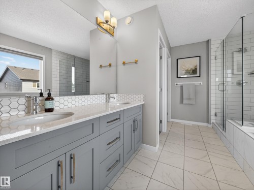 Bathroom featuring a dual vanity with grey cabinetry, a tiled backsplash, and a glass-enclosed shower and tub - 3210 Chernowski Way, Edmonton, AB - Indoor Photo Showing Bathroom