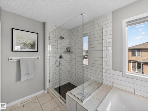 The bathroom features a spacious glass-enclosed shower with subway tile, a built-in shelf, and a window providing natural light - 3210 Chernowski Way, Edmonton, AB - Indoor Photo Showing Bathroom