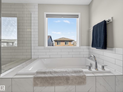 The bathroom features a built-in bathtub with polished chrome fixtures, white subway tile surround, and a clear glass shower enclosure - 3210 Chernowski Way, Edmonton, AB - Indoor Photo Showing Bathroom