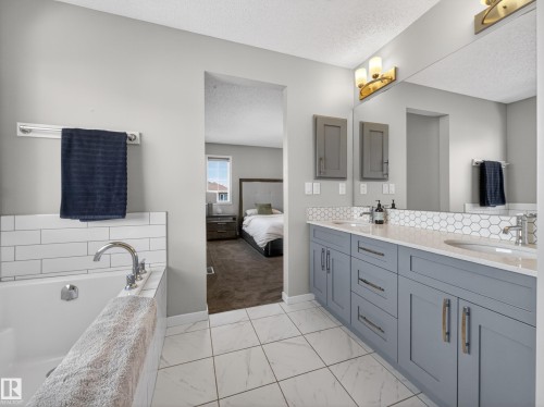 The bathroom features a deep soaking tub with subway tile surround, a spacious double vanity with shaker style cabinetry, and a large mirror with overhead lighting - 3210 Chernowski Way, Edmonton, AB - Indoor Photo Showing Bathroom