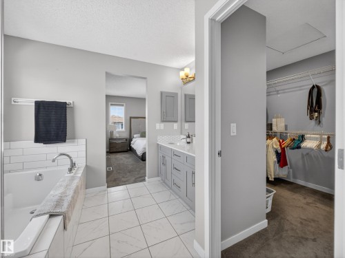 The property features a bathroom with a built-in bathtub, white subway tile surround, and a vanity with gray cabinetry and dual mirrors - 3210 Chernowski Way, Edmonton, AB - Indoor Photo Showing Bathroom
