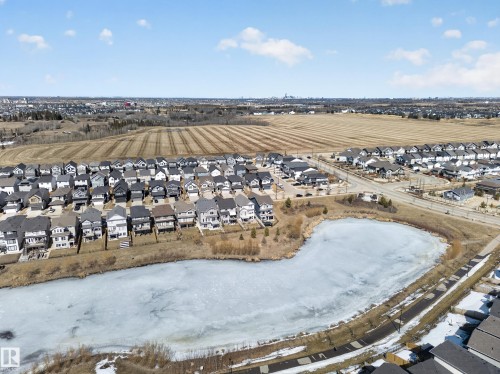 Aerial view of a residential neighbourhood featuring a body of water, several residential properties, and a cultivated field in the distance - 3210 Chernowski Way, Edmonton, AB - Outdoor With View