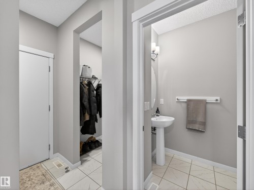 The property features a conveniently located powder room with a pedestal sink, an oval mirror, and wall-mounted lighting - 3210 Chernowski Way, Edmonton, AB - Indoor Photo Showing Bathroom