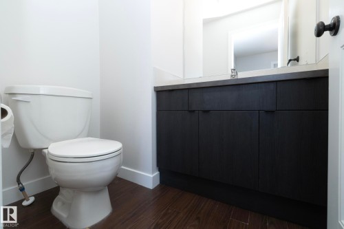 This bathroom features a white toilet, dark wood style flooring, and a vanity with a light countertop and dark cabinetry - 197 Birchwood Close, Devon, AB - Indoor Photo Showing Bathroom