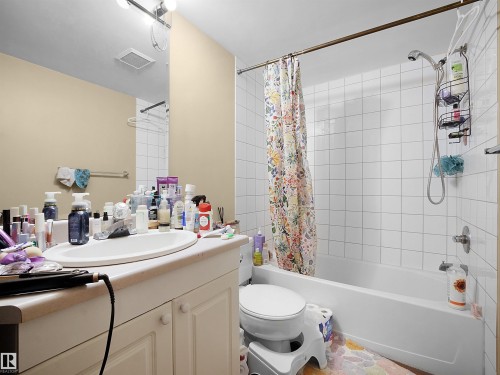 Bathroom featuring a vanity with an integrated sink, a large mirror, and a bathtub with white tile surround - 10 10331 106 Street, Edmonton, AB - Indoor Photo Showing Bathroom