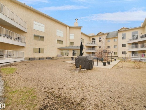 The property features a large outdoor space with a paved patio area, complete with an outdoor umbrella and seating - 10 10331 106 Street, Edmonton, AB - Outdoor