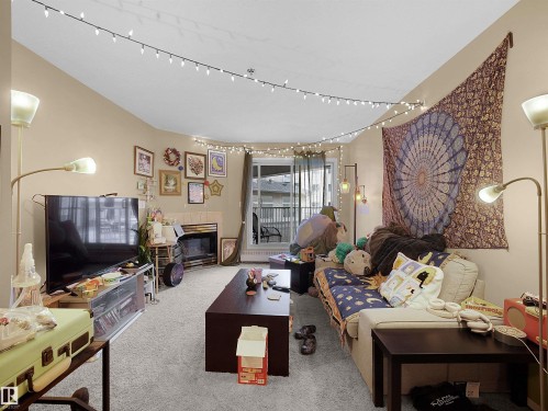 Living area featuring light-colored carpeting, a fireplace, and a glass sliding door leading to an outdoor space - 10 10331 106 Street, Edmonton, AB - Indoor Photo Showing Living Room With Fireplace