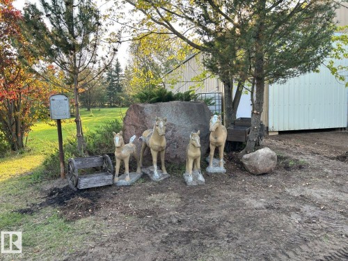 The property features an extensive outdoor area with mature trees and a large boulder, alongside decorative elements including horse statues and a wooden cart - Lot 118 Homestead Trail, Rural St. Paul County, AB 