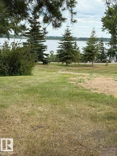 The property features a spacious lawn with evergreen trees and a view of a body of water in the distance - Lot 118 Homestead Trail, Rural St. Paul County, AB 