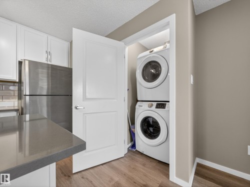 The property features a kitchen with white cabinetry, a stainless steel refrigerator, and a grey countertop - 124 148 Ebbers Boulevard, Edmonton, AB - Indoor Photo Showing Laundry Room