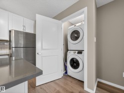 The property features a kitchen with white cabinetry, a stainless steel refrigerator, and a grey countertop - 