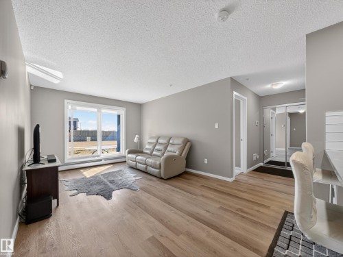 Living area featuring light wood flooring, light grey walls, and a large sliding glass door - 124 148 Ebbers Boulevard, Edmonton, AB - Indoor Photo Showing Living Room