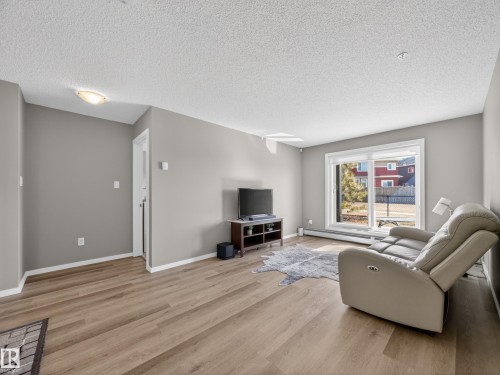 The living room features light wood-style flooring, light grey walls, and a sliding glass door leading to the outdoors - 124 148 Ebbers Boulevard, Edmonton, AB - Indoor Photo Showing Living Room