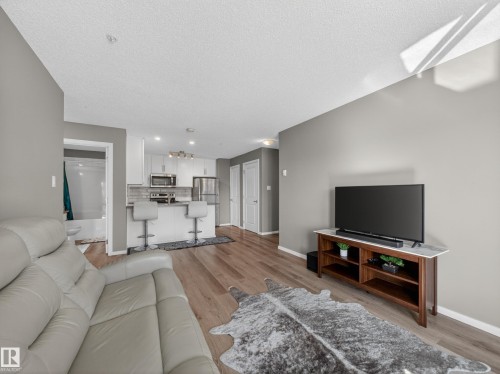 The property features hardwood floors, a kitchen with stainless steel appliances, and a breakfast bar with seating - 124 148 Ebbers Boulevard, Edmonton, AB - Indoor Photo Showing Living Room