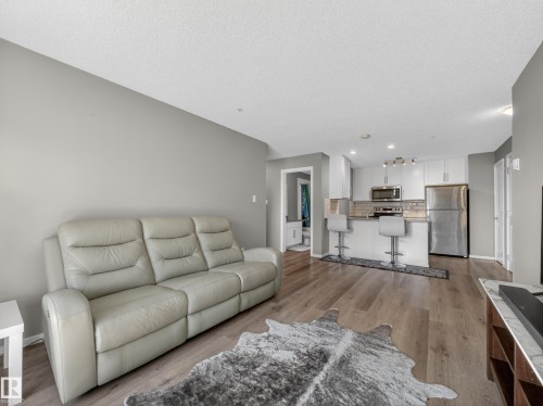 Open concept living area featuring engineered hardwood flooring and a kitchen equipped with stainless steel appliances, white cabinetry, and a subway tile backsplash - 124 148 Ebbers Boulevard, Edmonton, AB - Indoor Photo Showing Living Room