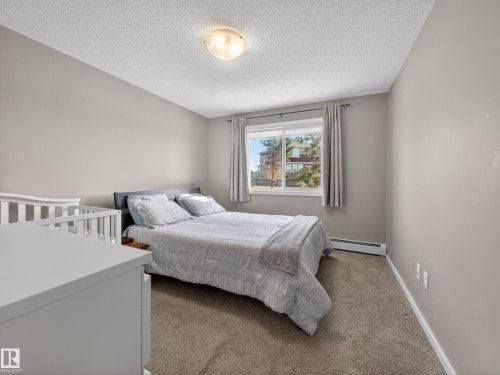 Bedroom featuring a window with a view of external buildings and trees, a ceiling light fixture, and carpeted flooring - 124 148 Ebbers Boulevard, Edmonton, AB - Indoor Photo Showing Bedroom