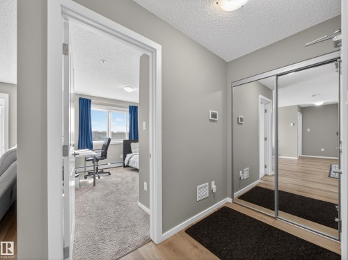This property features light wood flooring, a mirrored closet, and a room with carpeted flooring and large windows - 124 148 Ebbers Boulevard, Edmonton, AB - Indoor Photo Showing Other Room