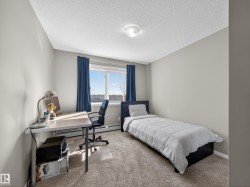 The room features light gray walls, carpeted flooring, and a window with blue curtains, allowing for natural light - 