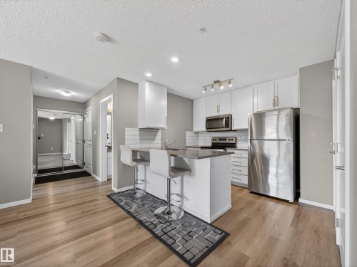 The property features a kitchen with white cabinetry, stainless steel appliances, and a kitchen island with seating - 124 148 Ebbers Boulevard, Edmonton, AB - Indoor Photo Showing Kitchen With Stainless Steel Kitchen With Upgraded Kitchen