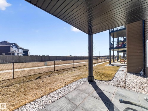 This property features an outdoor patio with concrete pavers and white gravel, leading to a lawn area with a chain link fence - 124 148 Ebbers Boulevard, Edmonton, AB - Outdoor