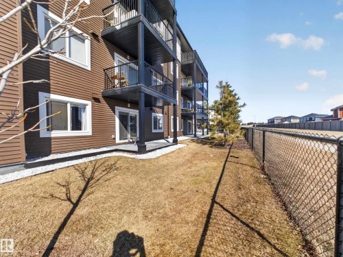 The property features a brown exterior with white trim windows and glass sliding doors leading to a patio area - 124 148 Ebbers Boulevard, Edmonton, AB - Outdoor