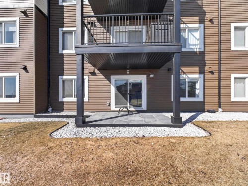 The property features a ground-level patio with a sliding glass door entry, bordered by decorative gravel and a natural grass area - 124 148 Ebbers Boulevard, Edmonton, AB - Outdoor With Exterior