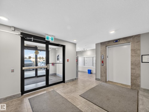The property features a bright entrance with glass doors, leading to a common area with an elevator and mailboxes, all set on tiled flooring - 124 148 Ebbers Boulevard, Edmonton, AB - Indoor Photo Showing Other Room