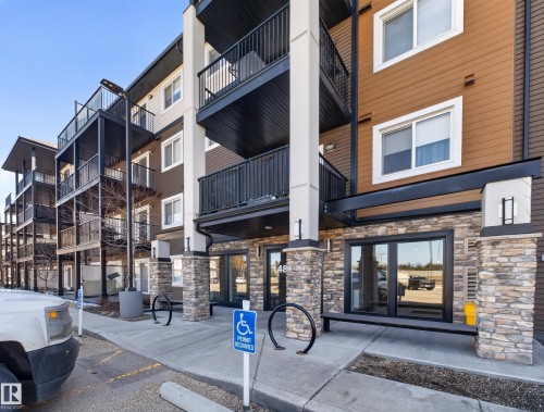 The property features a modern exterior with brown and tan siding, accented by stone veneer columns and a black railing system - 124 148 Ebbers Boulevard, Edmonton, AB - Outdoor