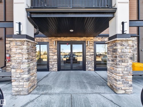 The property features an entrance with stone pillar accents, large glass doors, and exterior lighting fixtures - 124 148 Ebbers Boulevard, Edmonton, AB - Outdoor