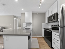 The kitchen features white cabinetry, stainless steel appliances, a grey countertop, and a white subway tile backsplash - 