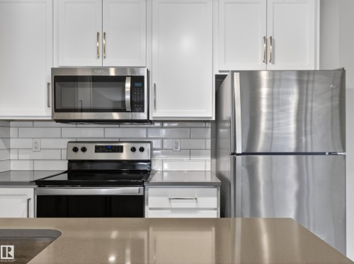 The kitchen features white cabinetry, stainless steel appliances including a microwave, refrigerator, and range, and a subway tile backsplash - 124 148 Ebbers Boulevard, Edmonton, AB - Indoor Photo Showing Kitchen With Stainless Steel Kitchen With Upgraded Kitchen