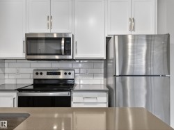 The kitchen features white cabinetry, stainless steel appliances including a microwave, refrigerator, and range, and a subway tile backsplash - 