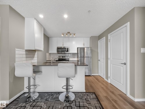 The property features a kitchen with white cabinetry, stainless steel appliances, a tiled backsplash, and recessed lighting - 124 148 Ebbers Boulevard, Edmonton, AB - Indoor Photo Showing Kitchen