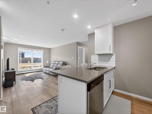 The property features an open living area with wood-style flooring and a sliding glass door providing natural light - 124 148 Ebbers Boulevard, Edmonton, AB - Indoor Photo Showing Kitchen With Double Sink