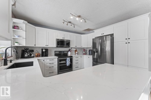 The kitchen features white cabinetry, a white quartz countertop, and stainless steel appliances, including a microwavehood fan, stove, dishwasher, and refrigerator - 1929 Forest Drive, Cold Lake, AB - Indoor Photo Showing Kitchen