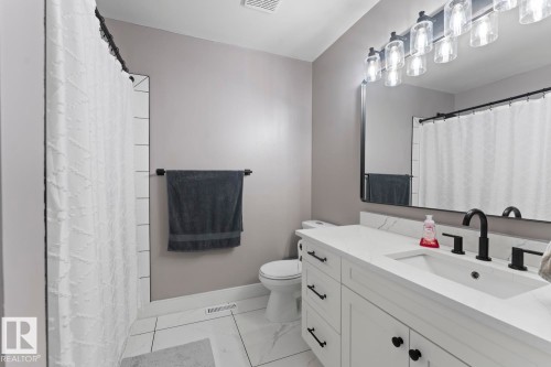 Bathroom featuring a white vanity with a white quartz countertop and black fixtures, and a white tiled surround bathtub - 1929 Forest Drive, Cold Lake, AB - Indoor Photo Showing Bathroom